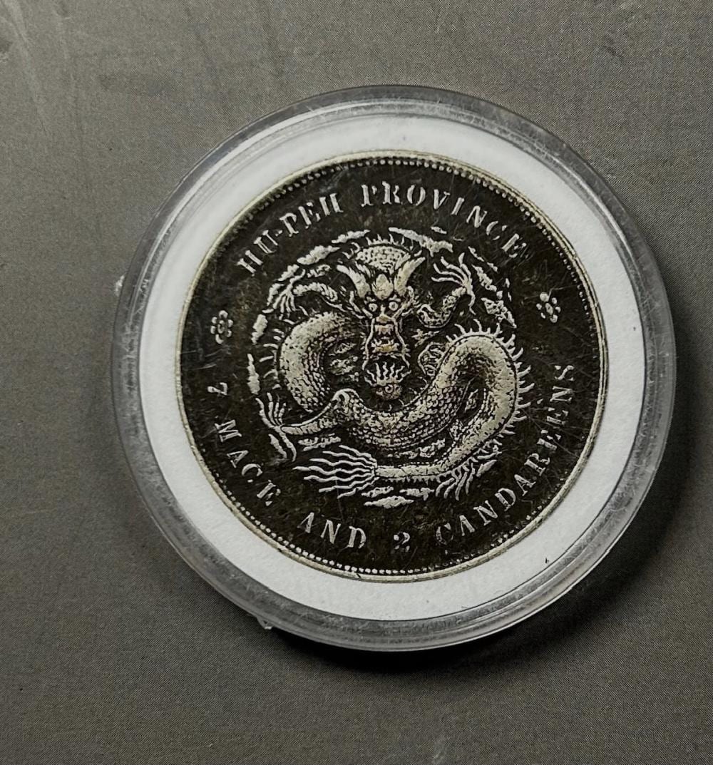Close-up of a round coin featuring a detailed dragon design in the center and engraved text around the border.