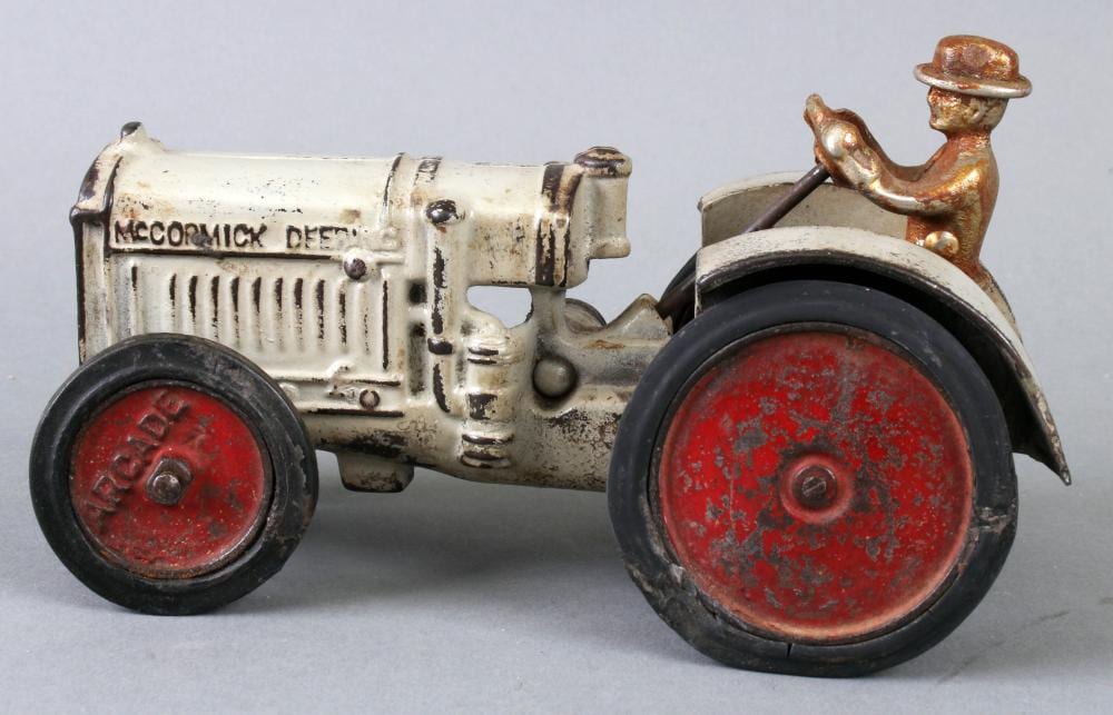 Cast iron toy tractor with white body, red wheels, and a seated driver figure wearing a brown hat.