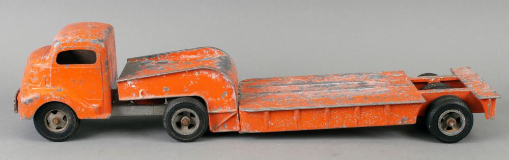 Orange toy truck with a long flatbed trailer and black wheels, shown in side view against a light background.