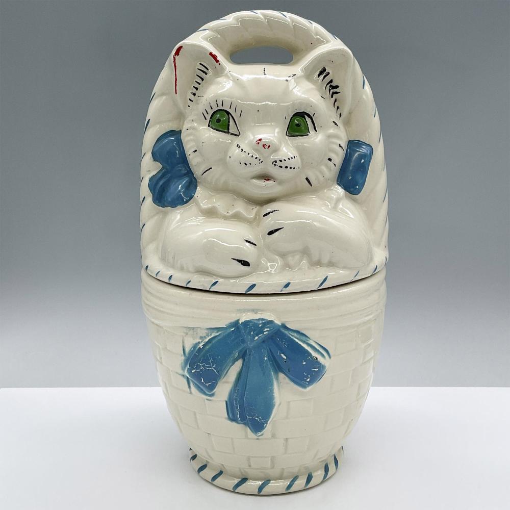 Ceramic cat cookie jar with a lid shaped like a cat’s head, painted white with green eyes and blue ears and paws.