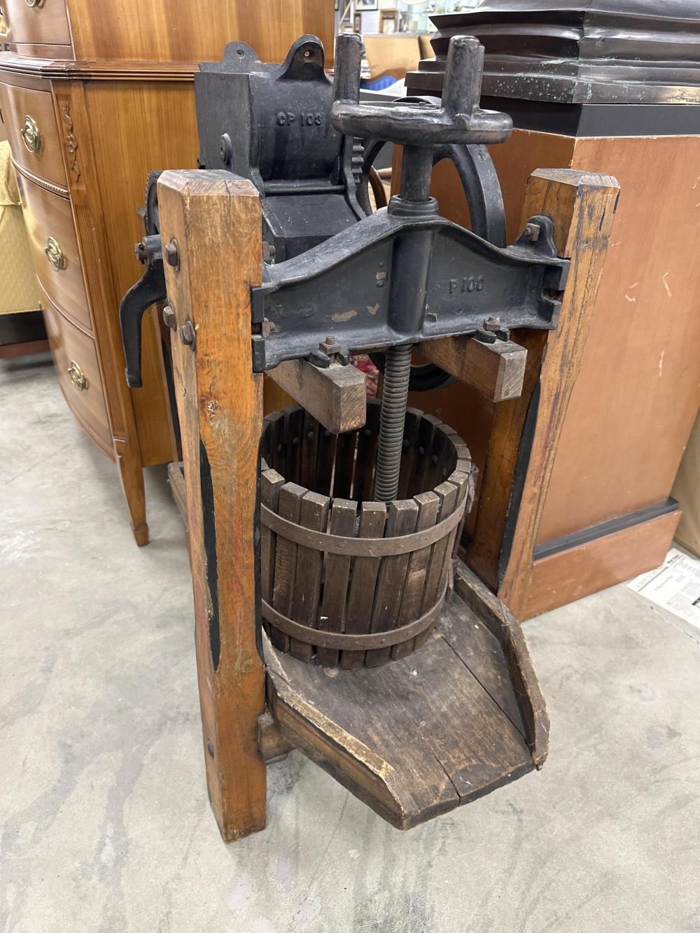 Vintage cider press machine with a wooden frame, cast-iron press mechanism, and a barrel-like wood press basket.