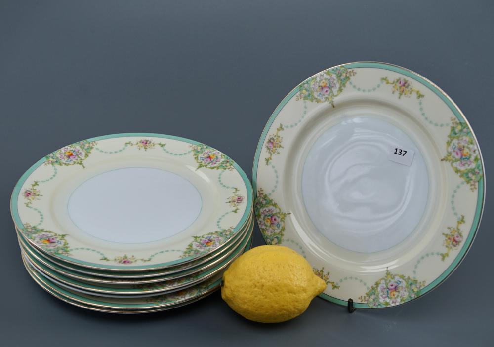 Two decorative ceramic salad plates with green and floral garden pattern on a pale rim, photographed on a gray background.