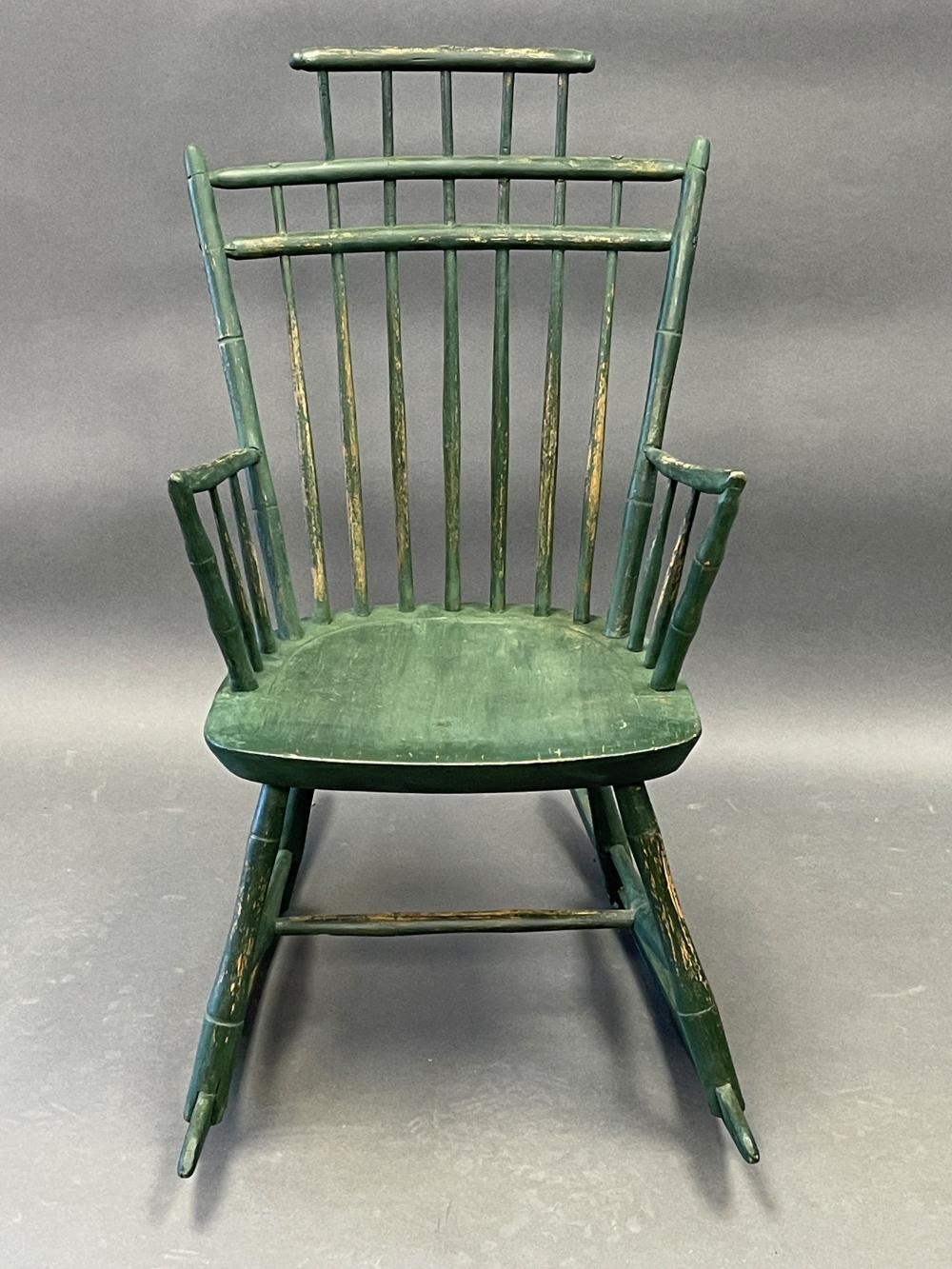 Green wooden rocking chair with vertical slat back and rounded seat, viewed straight-on in a studio setting.
