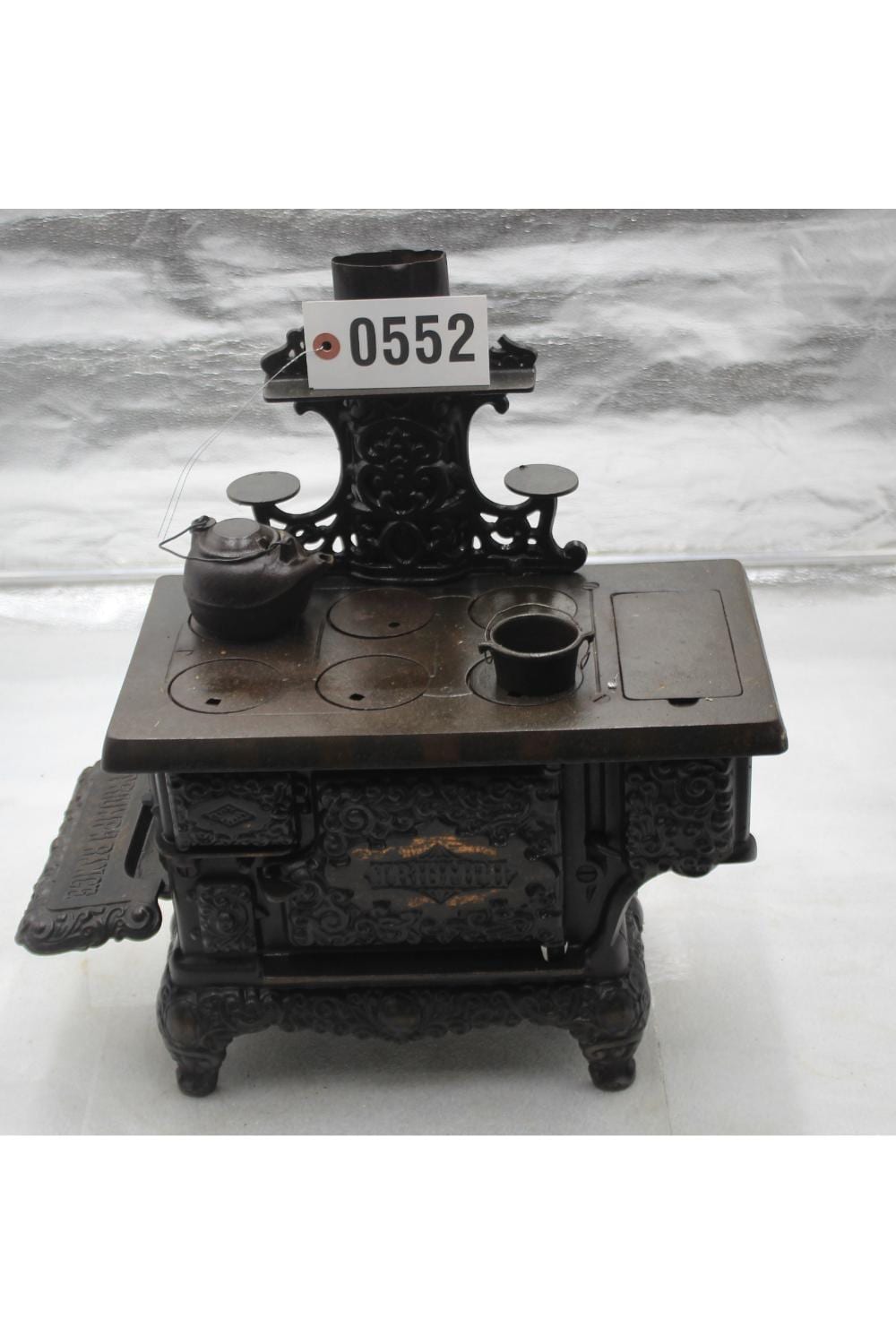 Black cast-iron toy stove with embossed front panels, three circular openings on the top, and small pots and lids on the counter.
