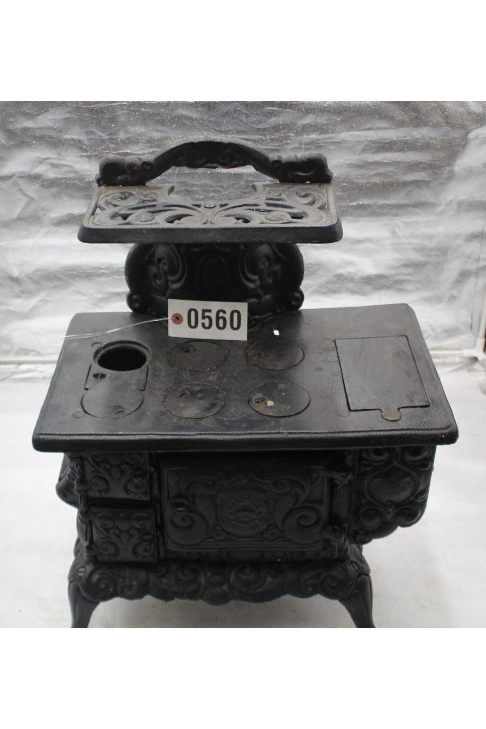Black cast-iron toy stove with a decorated front panel and a flat top with circular openings and a handle.
