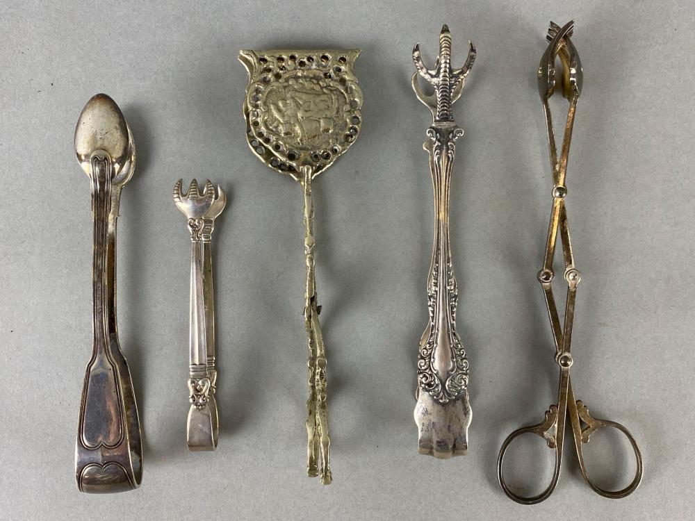 Five metal ice tongs arranged side by side, each with ornate handles and claw-like ends, photographed against a gray background.