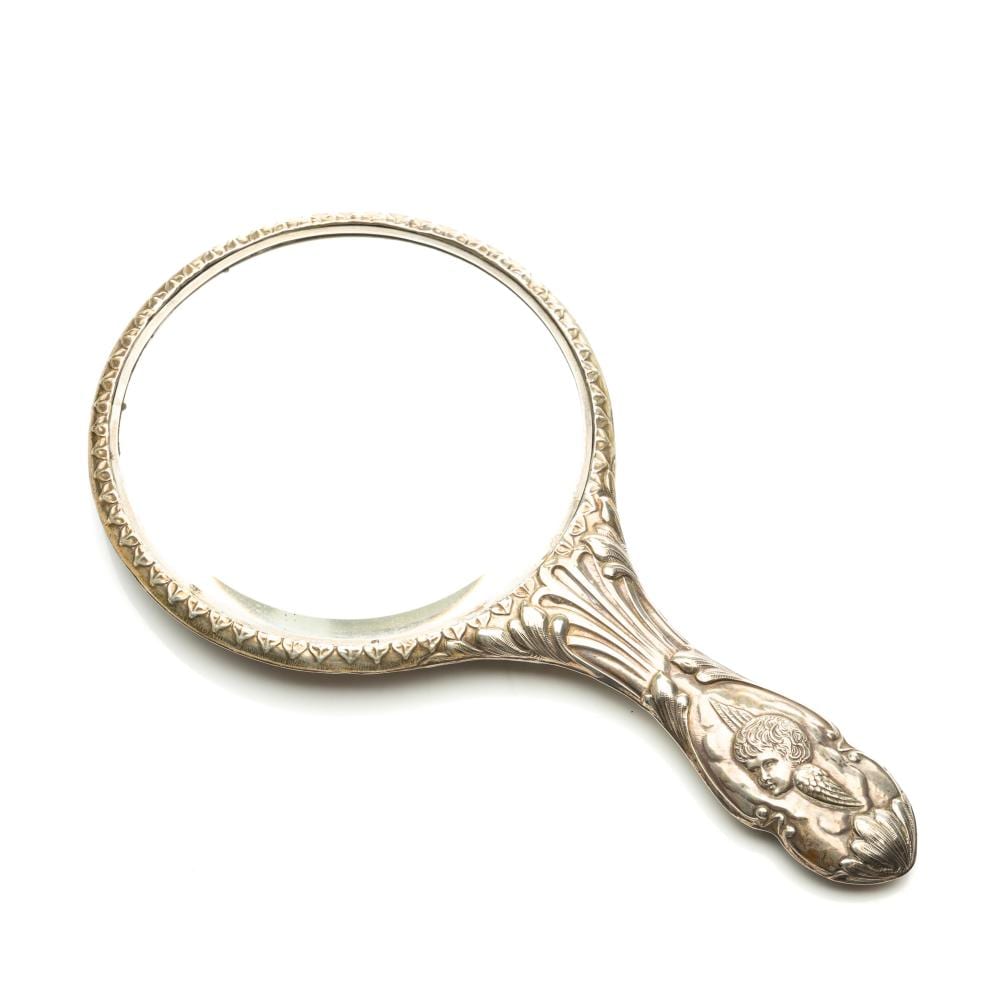 Ornate silver-tone hand mirror with a round reflective glass and embossed cherub decoration on the handle.