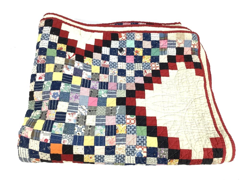 Vintage patchwork quilt with a multicolored checker pattern and red border, laid flat against a white background.