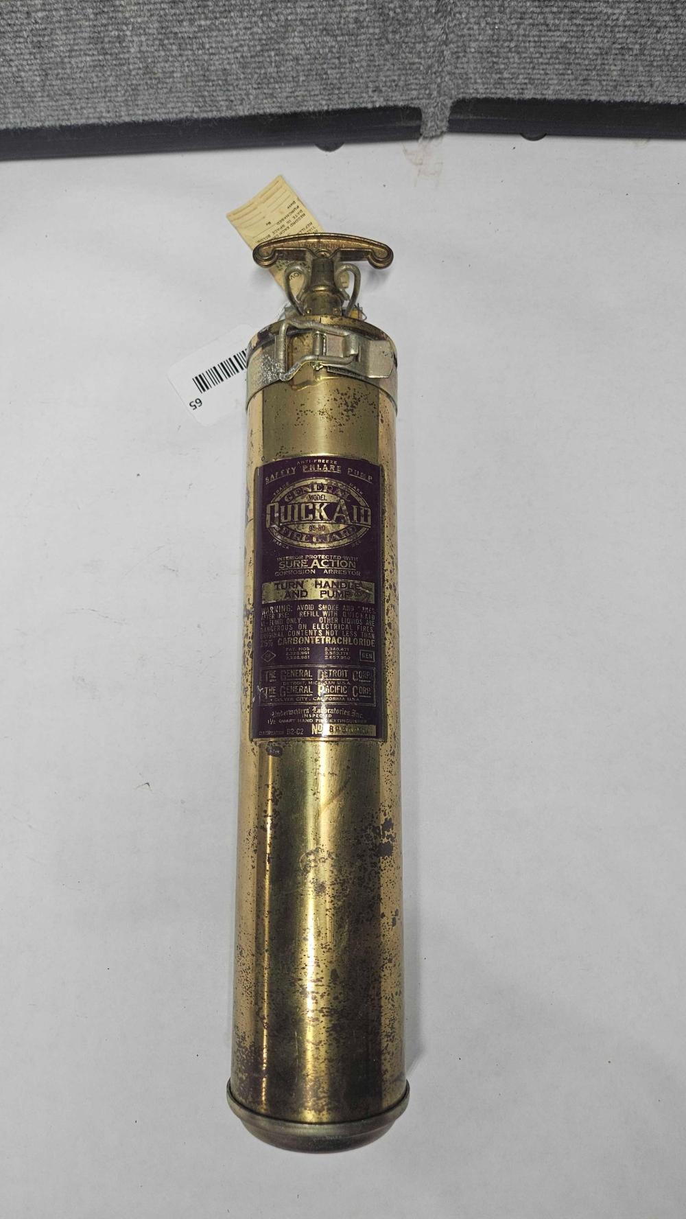 Brass fire extinguisher with a metal handle and nozzle mounted on top, shown upright against a gray background.