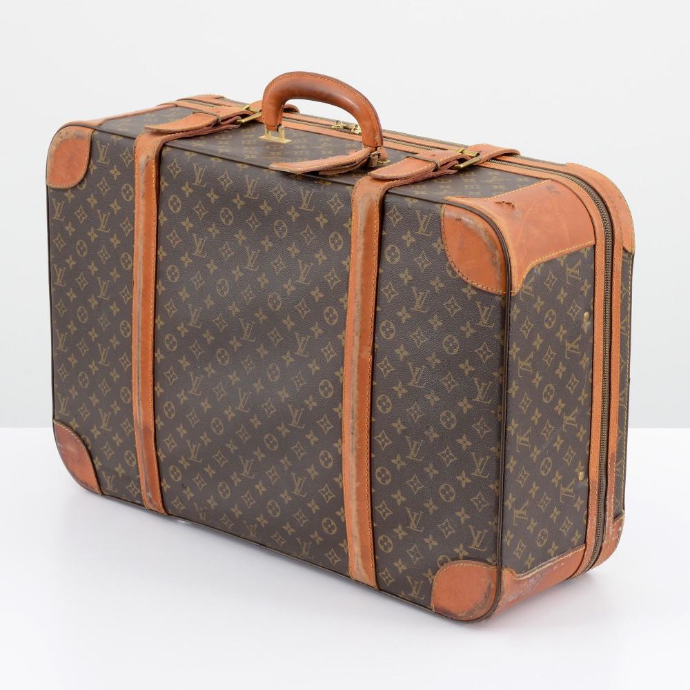 Brown monogram canvas suitcase with tan leather trim and handles, shown in a three-quarter view on a white background.