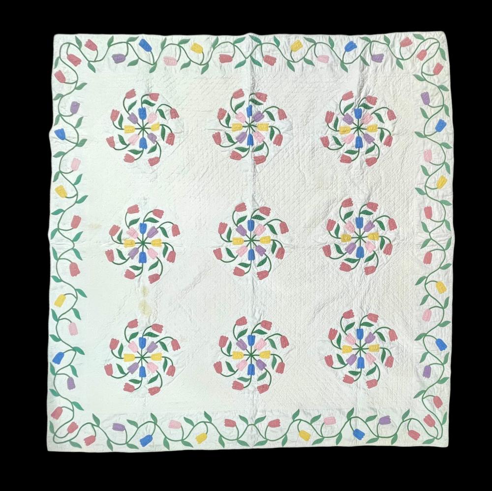 White quilt with colorful appliqué tulip-like floral blocks and a green leaf border.