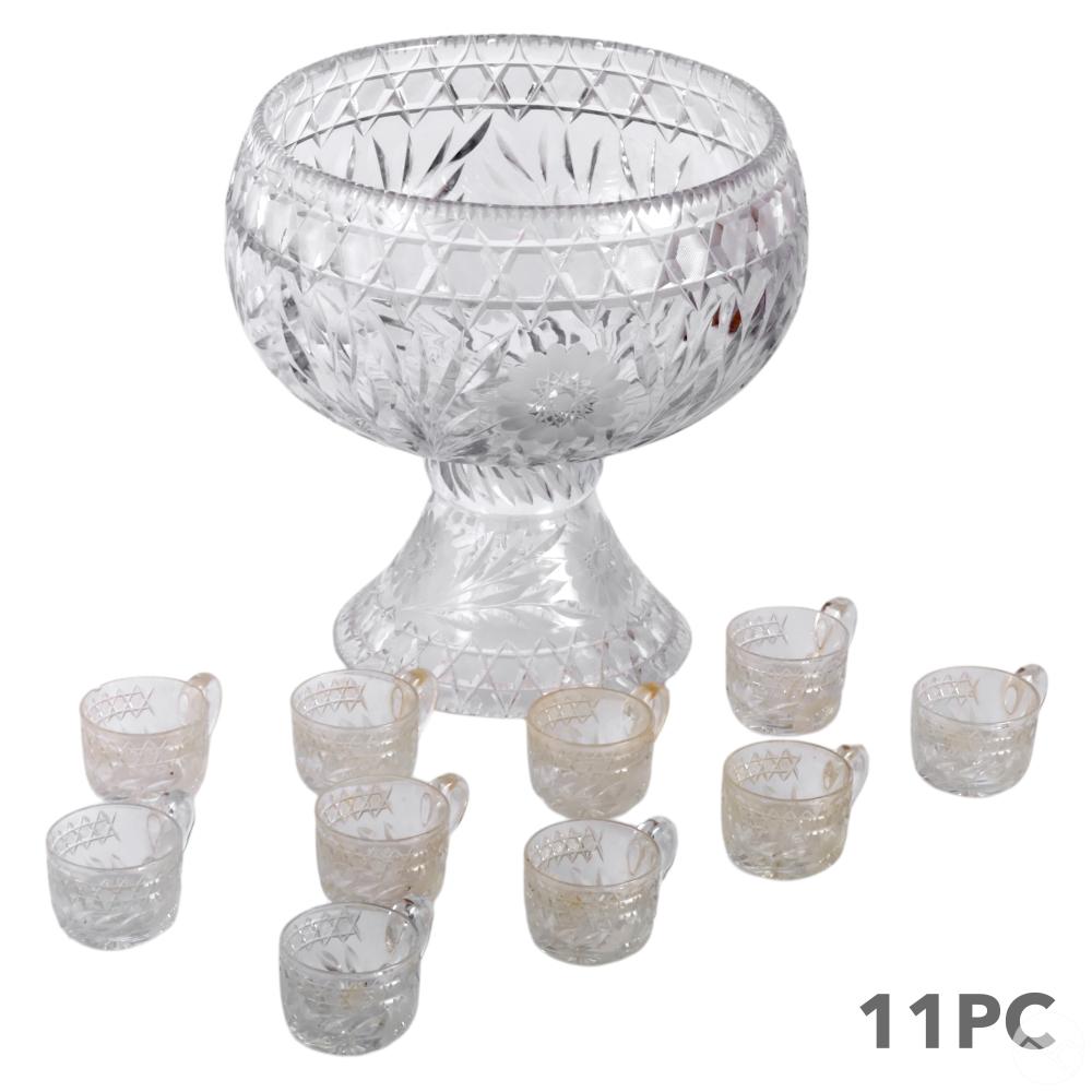 Clear cut-glass punch bowl with matching small glasses arranged around it on a white background.