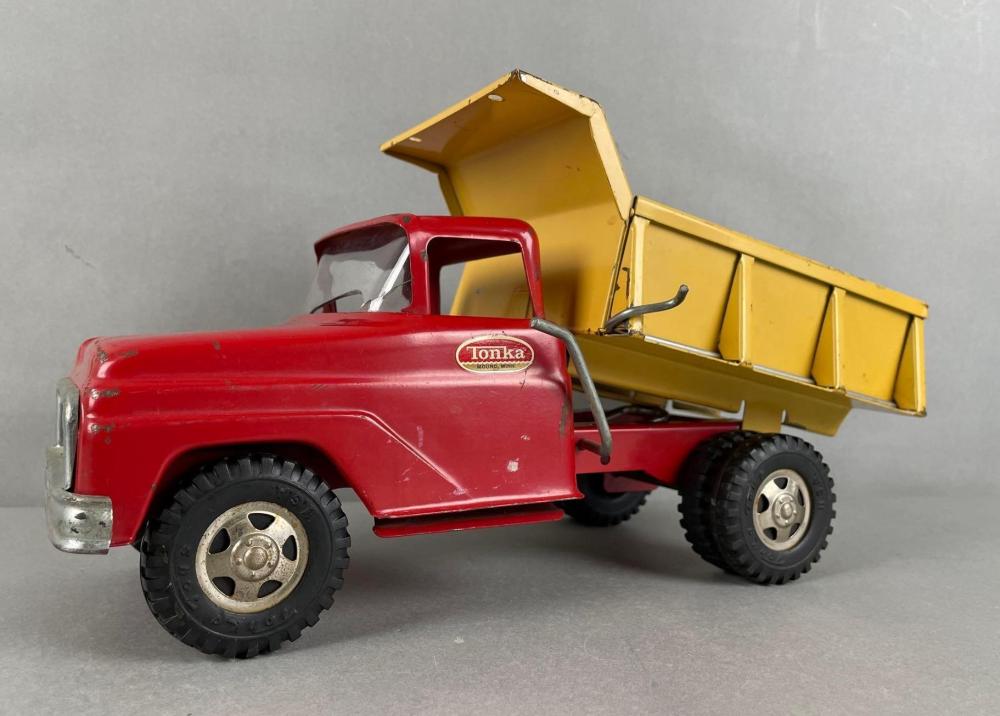 Red toy dump truck with yellow open cargo bed and black wheels, shown in profile on a light gray background.