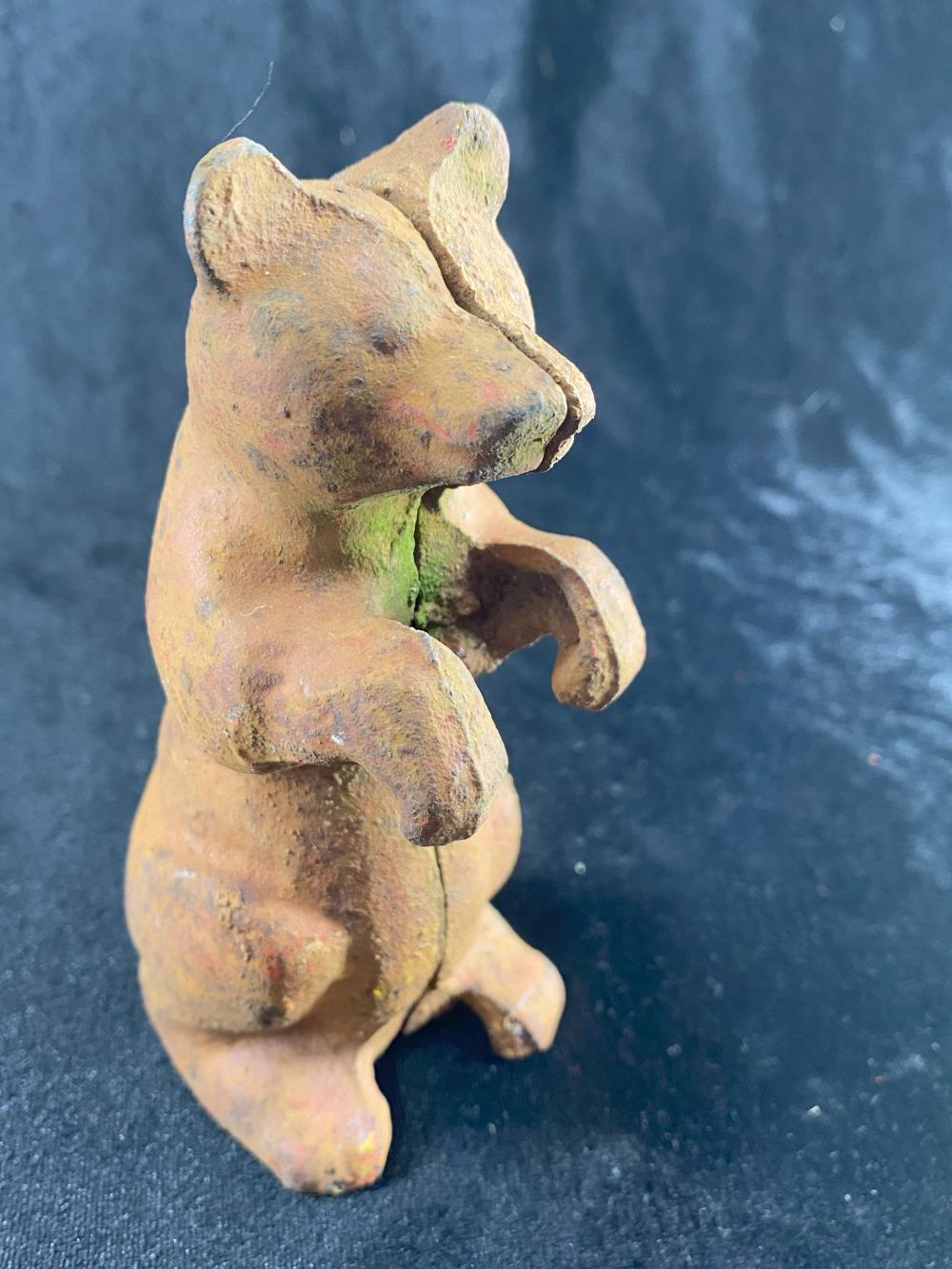Small cast-iron bear-shaped piggy bank figure with a coin slot in the back, shown against a dark blue fabric background.