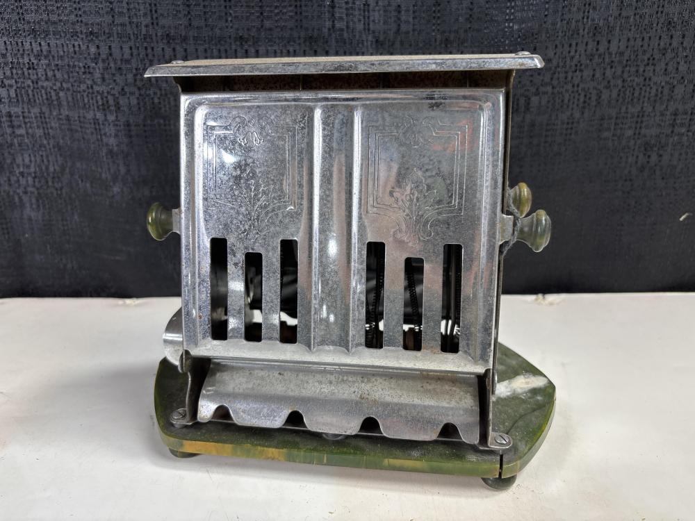 Vintage metal toaster with vented sides and a top rack, shown from the front on a green base.
