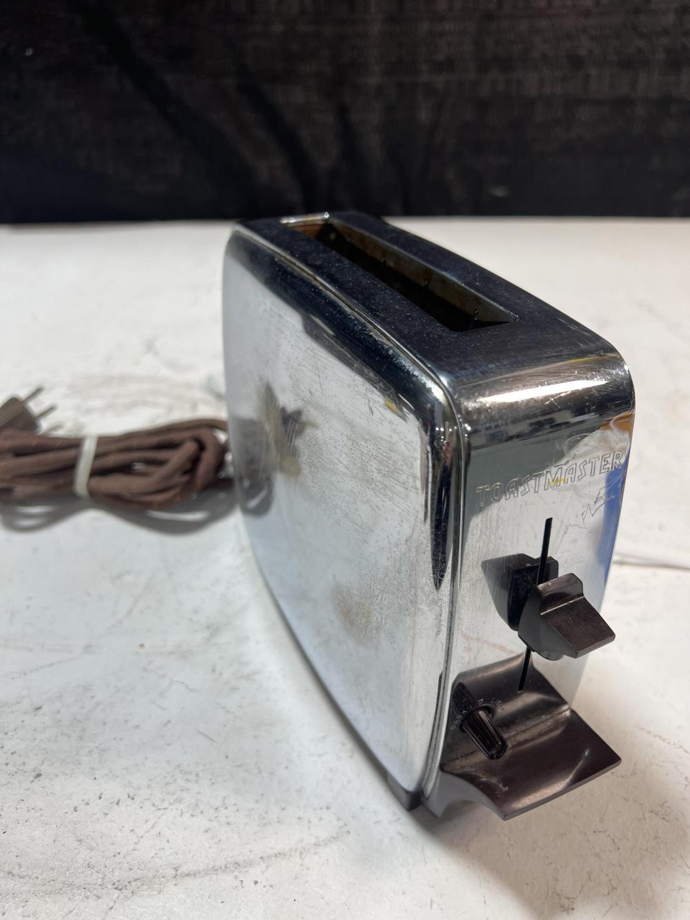 Chrome vintage single-slice pop-up toaster with dark top slot and side lever on a white surface.