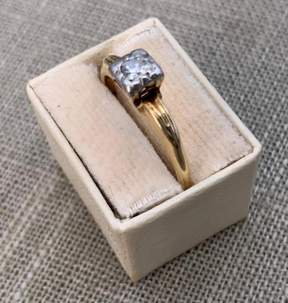 Close-up of a gold ring in a white jewelry box, featuring a round solitaire diamond set in prongs.