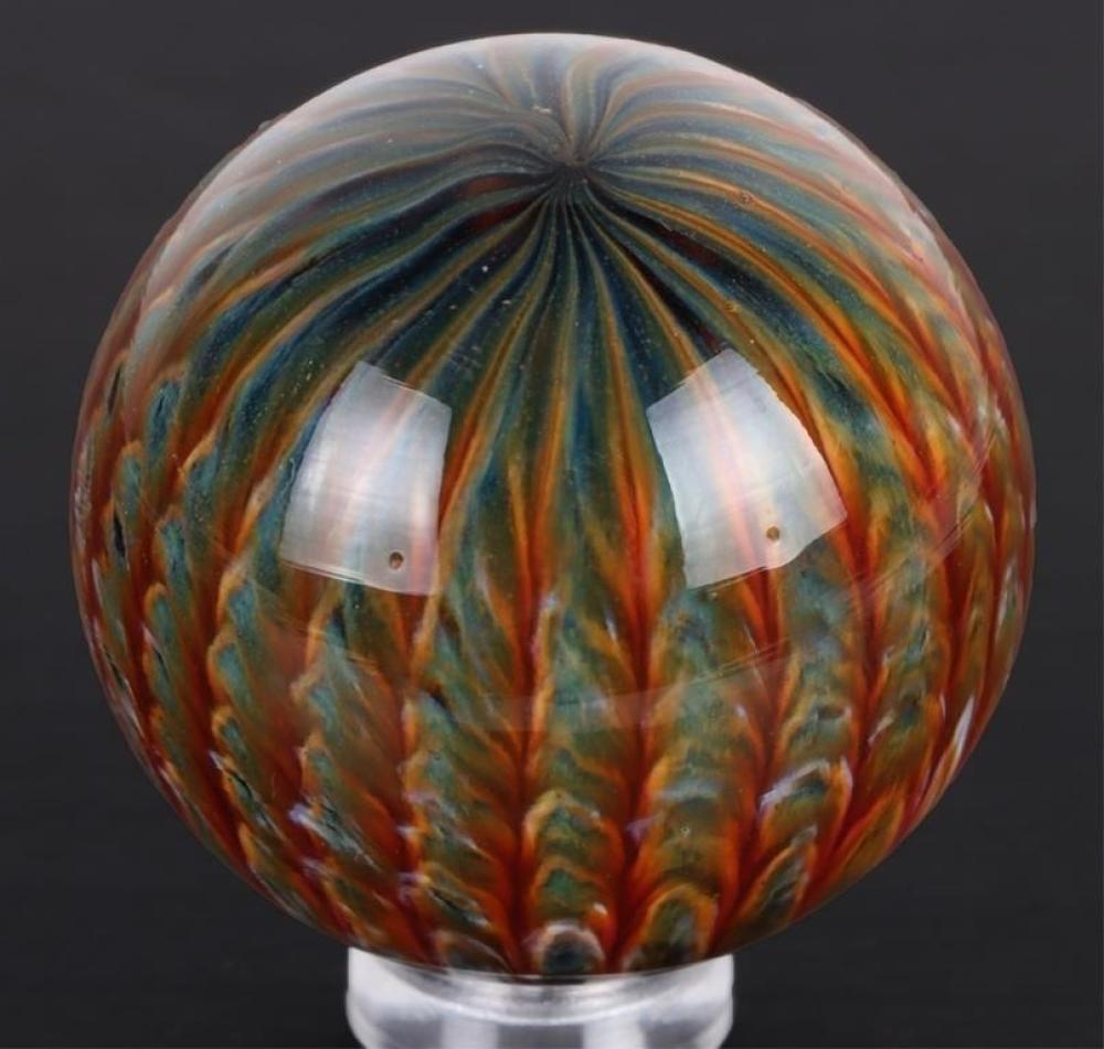Handmade glass marble with multicolored swirl stripes, photographed on a dark background and resting in a holder.