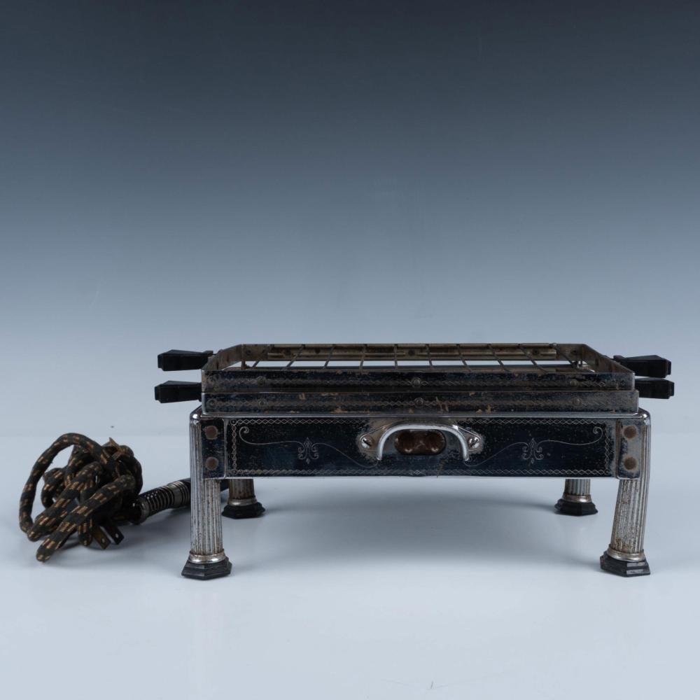 Vintage countertop toaster with dark body, decorative panel, and a handle at center on four legs; power cord and plug beside it.