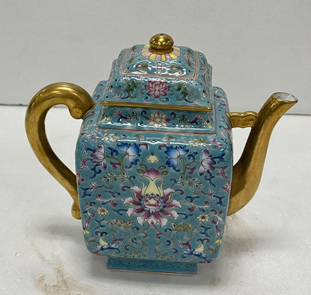 Blue porcelain teapot with gold handle and spout, decorated with colorful floral and scrolling patterns and a round gold lid knob.