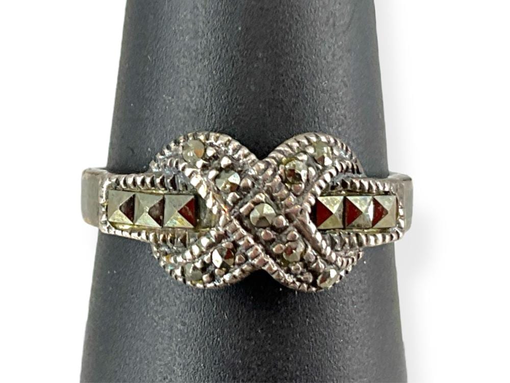 Silver ring with a central round light-colored stone and two side rows of small rectangular stones on a gray stand.