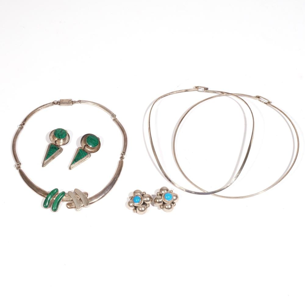 Set of silver-tone jewelry with hoop-like necklace chain, green enamel drop earrings, and blue-stone flower stud earrings arranged on a white background.