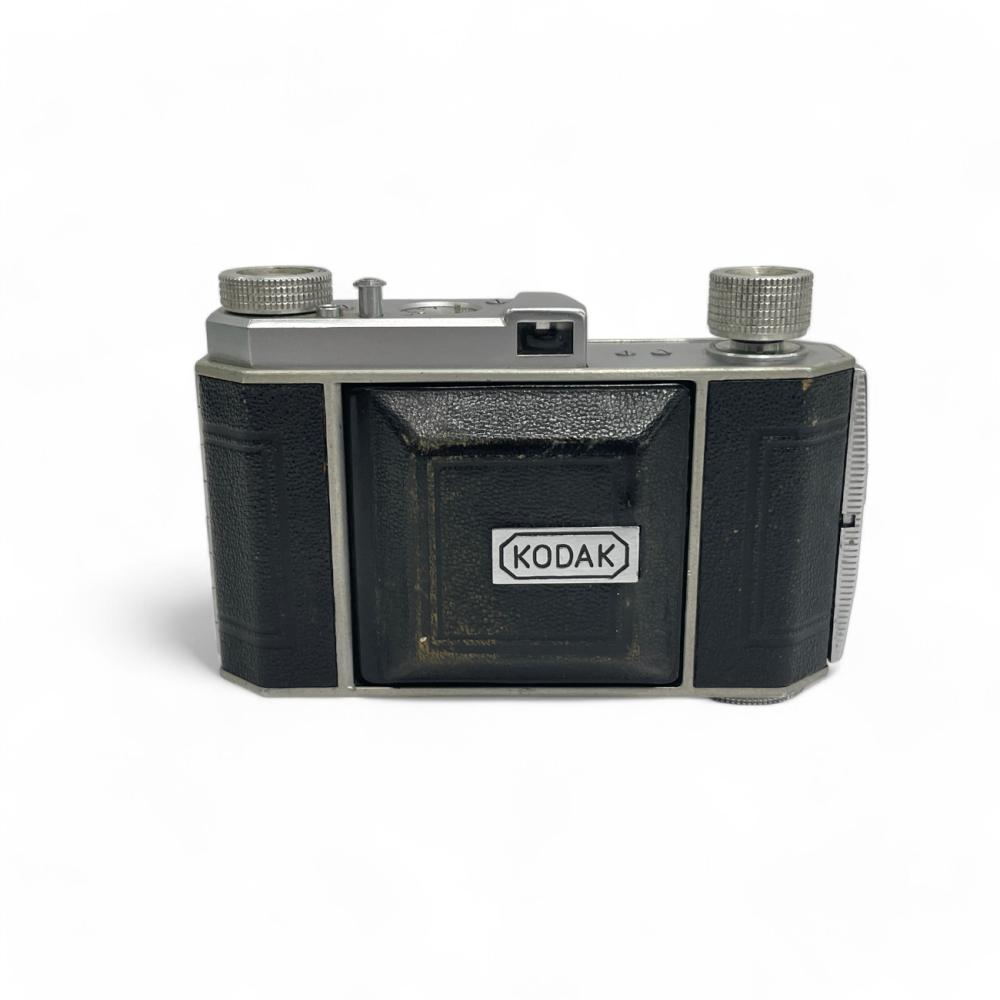 Front view of a vintage black Kodak camera with textured grips, silver top dials, and a visible Kodak label.