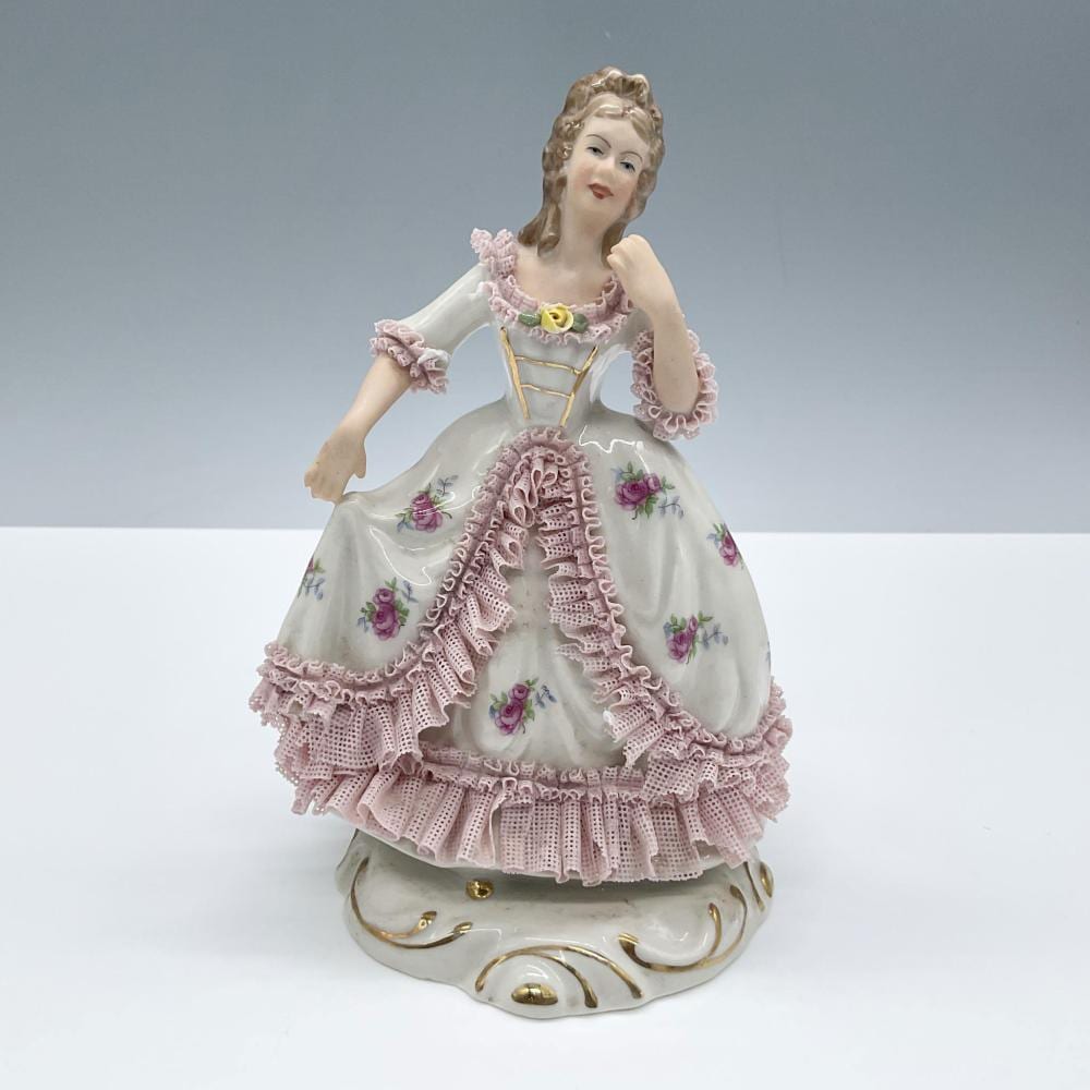 Porcelain figurine of a young woman in a white dress with pink lace ruffles and floral details, standing on a white base.