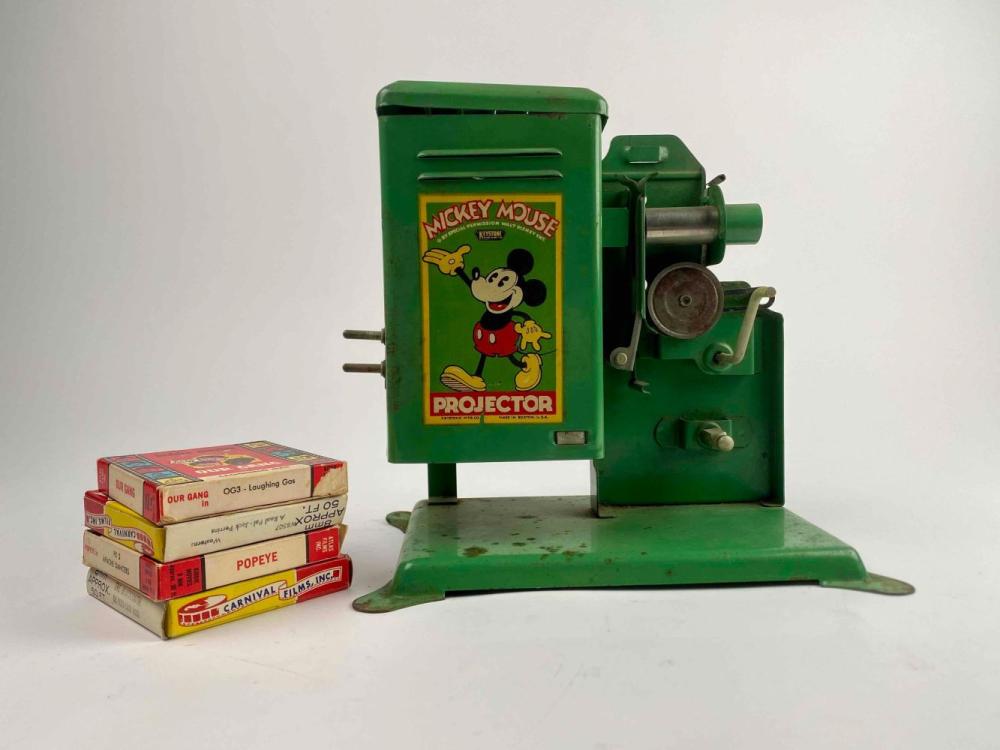 Green vintage film projector with Mickey Mouse label on the front, shown with several small boxed films beside it.