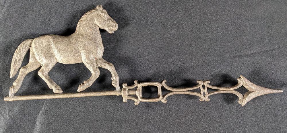 Metal horse weathervane silhouette with decorative scrollwork and a long horizontal mount against a dark background.