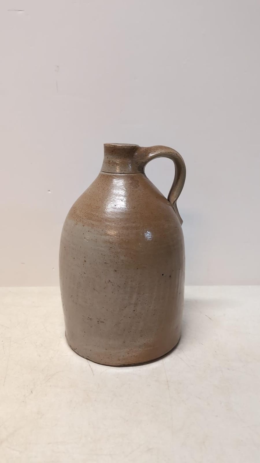 Brown stoneware crock jug with rounded body and curved handle, photographed against a plain light background.