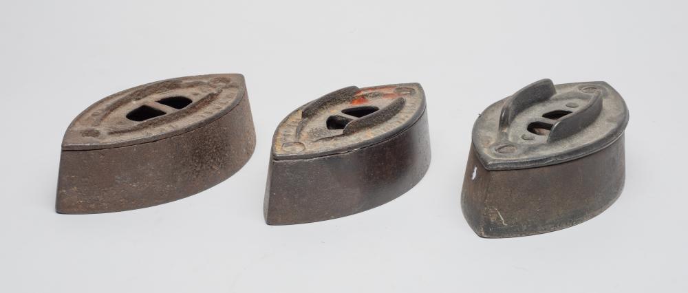 Three antique sad irons (cast-iron clothing irons) shown from above, with soleplates and steam holes.