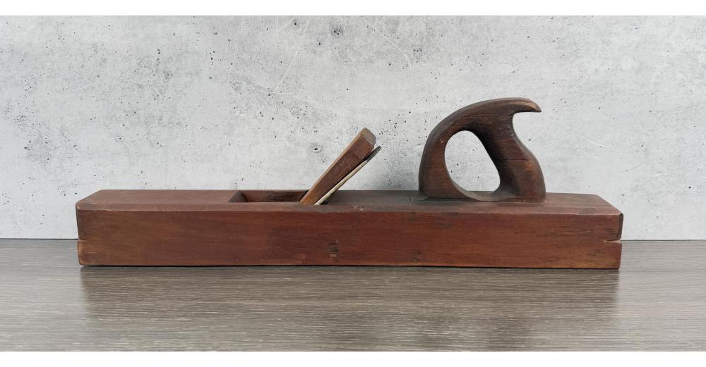 Antique-style wooden hand plane tool lying on a table, showing a curved handle and metal blade opening.