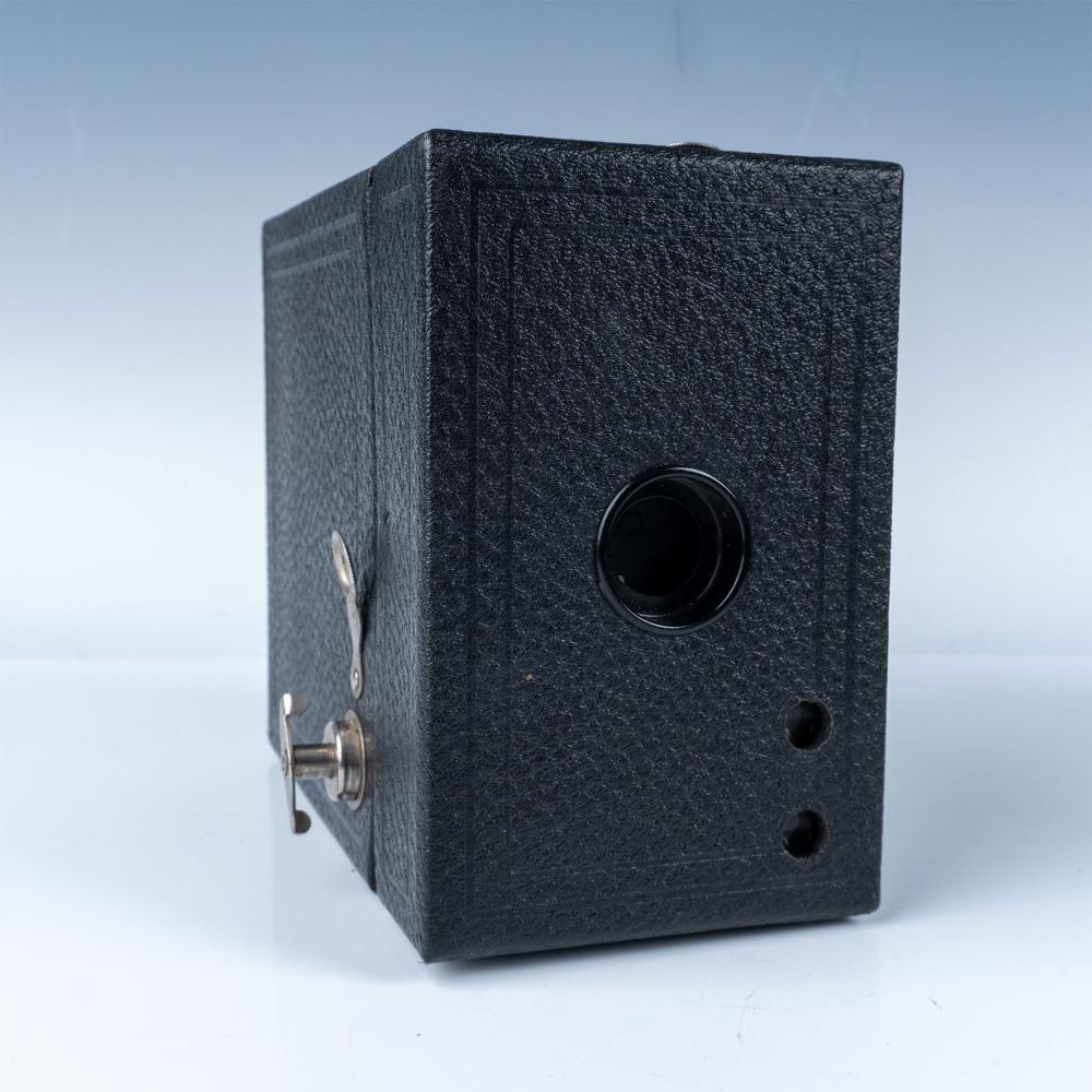 Black box-style camera with a round lens opening and metal shutter lever on the left side.