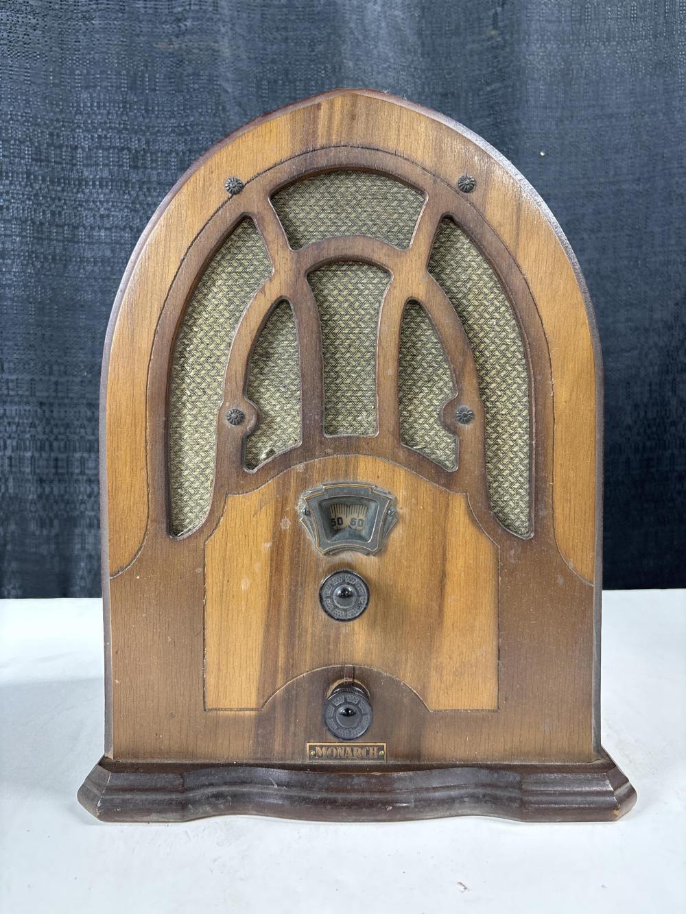 Front view of a vintage wooden cathedral-style radio with an arched speaker grille, tuning dial, and “MONARCH” badge.