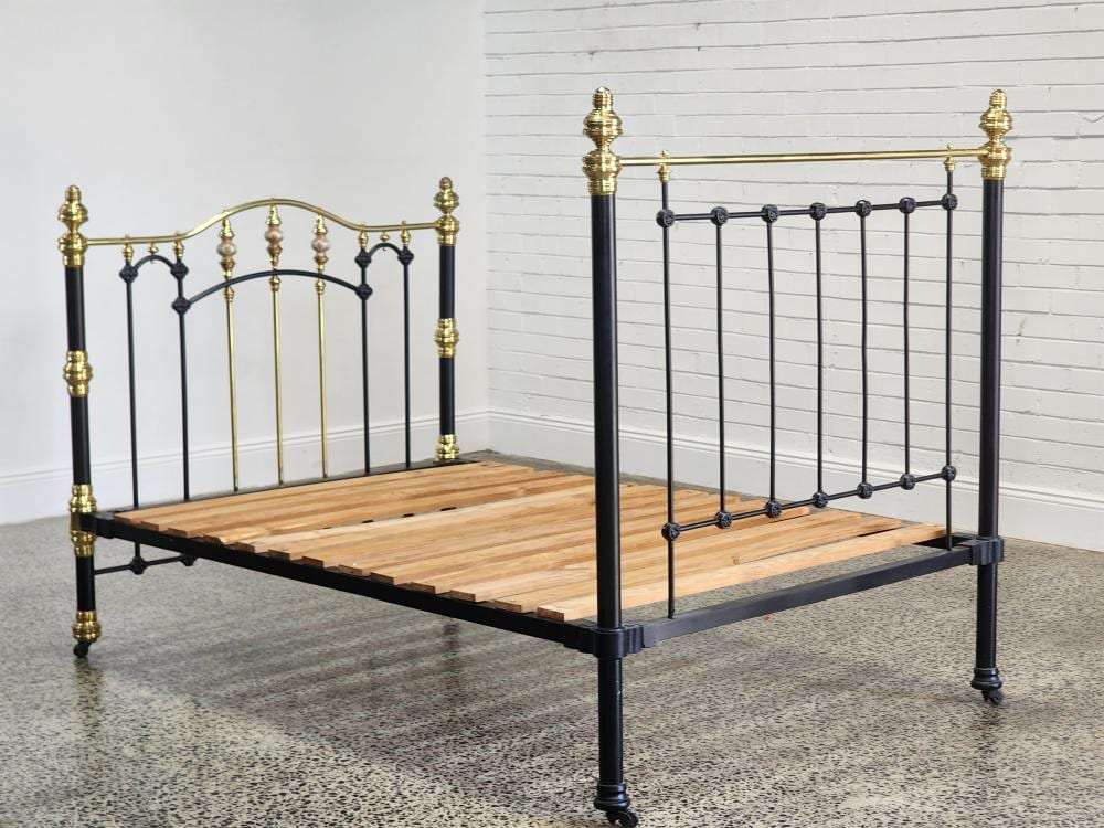 Antique-style metal bed frame with black posts and iron-and-brass finials, featuring a wooden slat base.
