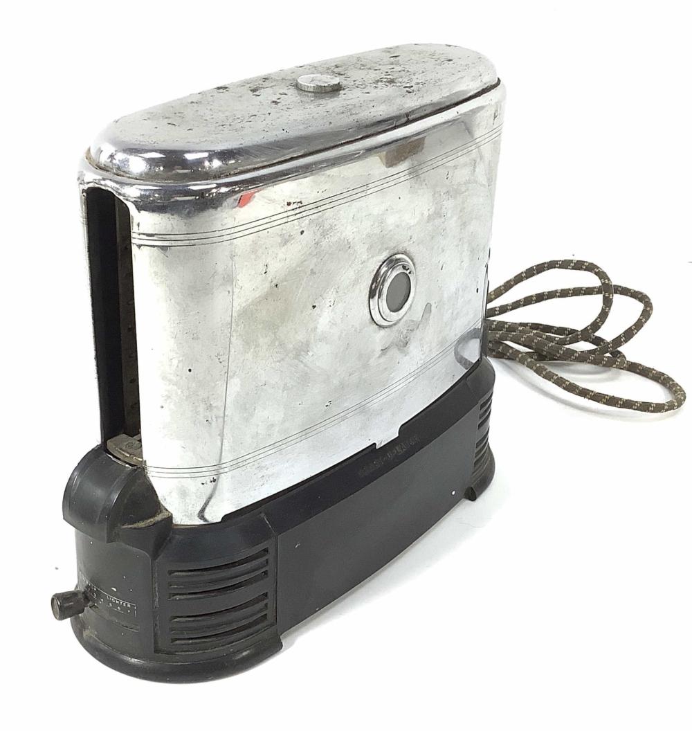 Vintage chrome toaster with a black base and a top cover, shown with its power cord coiled beside it.