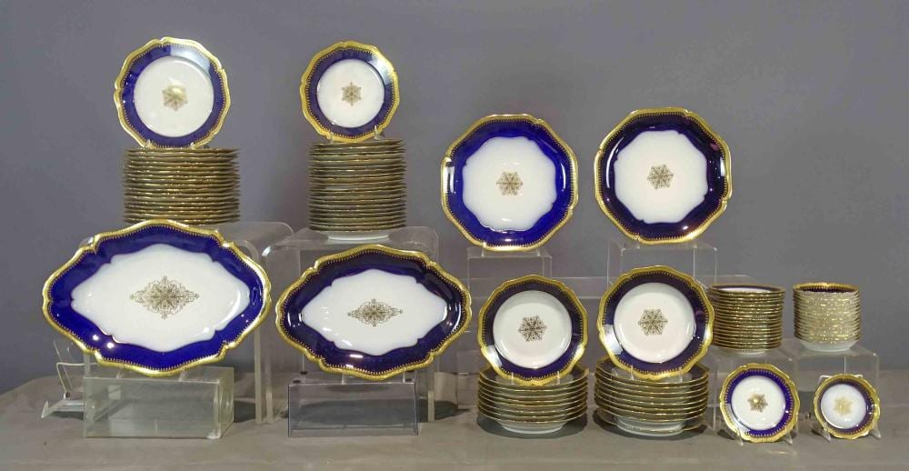 Set of gold-rimmed blue ceramic plates and bowls with small central floral medallions, arranged on display stands