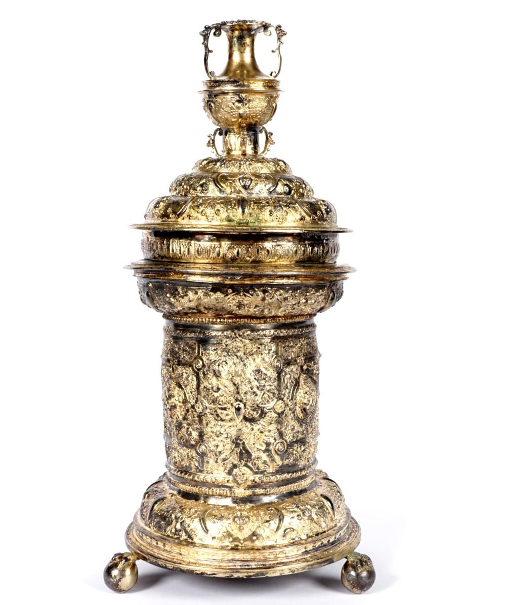 Ornate gold-tone metal salt cellar with tiered body, decorative bands, and handles on a white background.