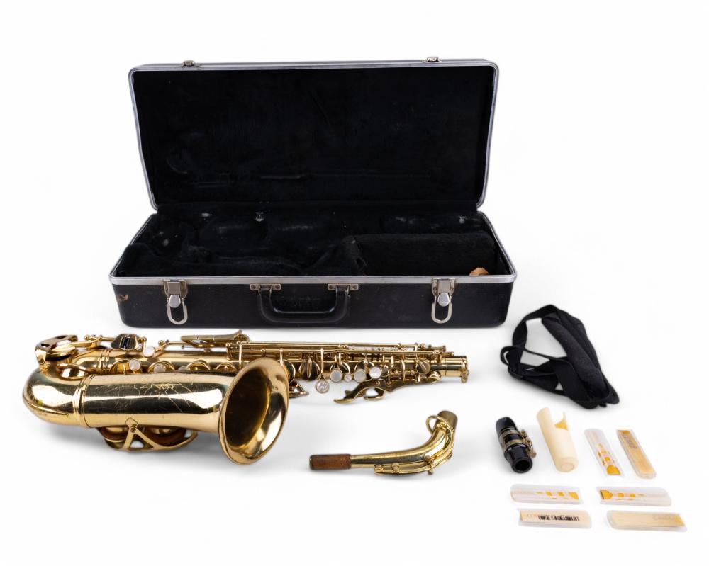 Gold alto saxophone with mouthpiece and mouthpiece accessories laid out beside a black hard case.