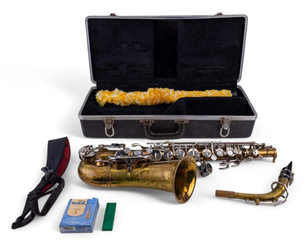 Open case showing an alto saxophone with brass body, silver keys, and detachable neck mouthpiece; includes a cleaning strap and small accessories.