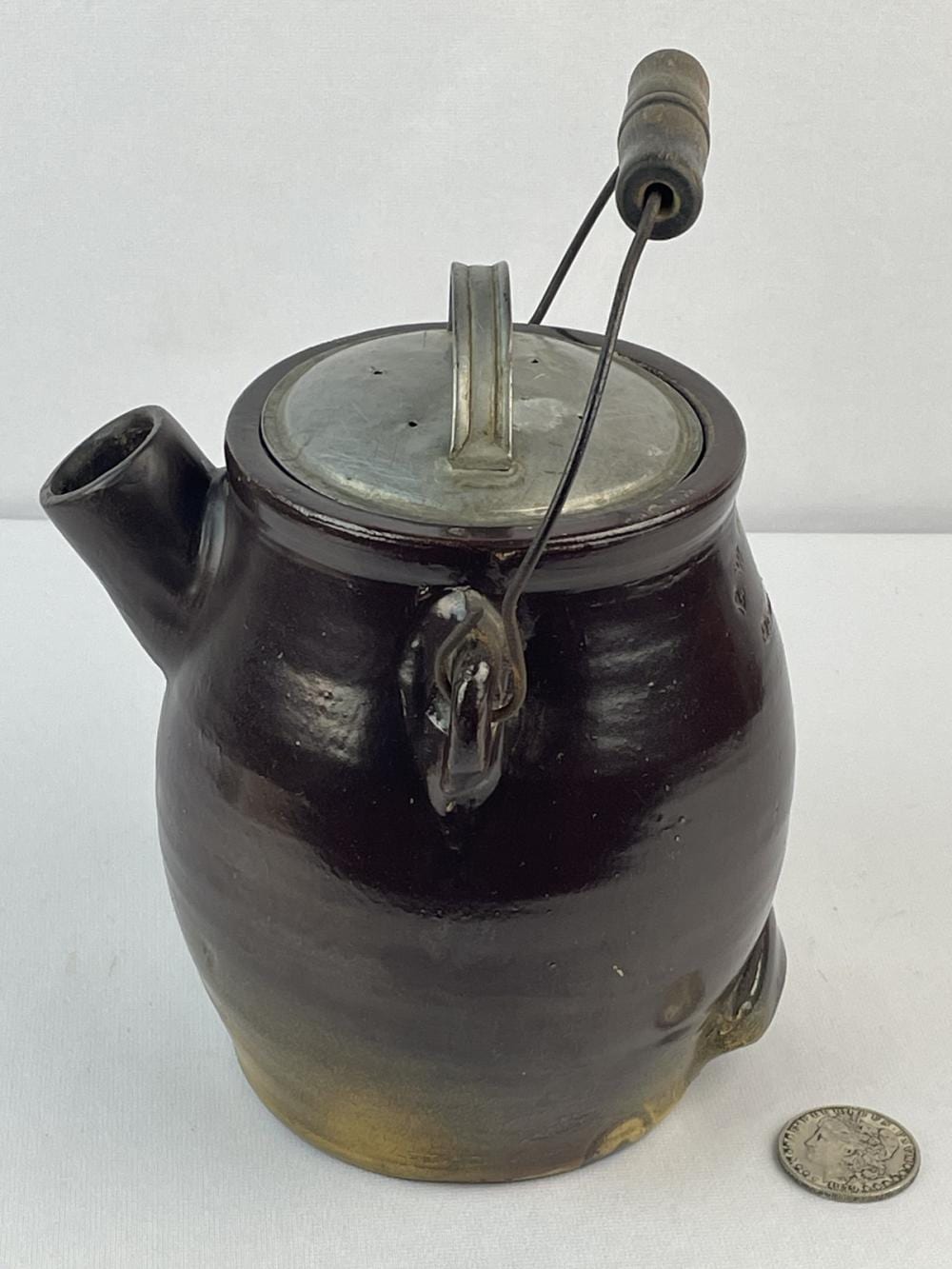 Brown stoneware batter jug with bail handle, hinged metal spout, and round lid; photographed on a light background next to a small coin for scale.