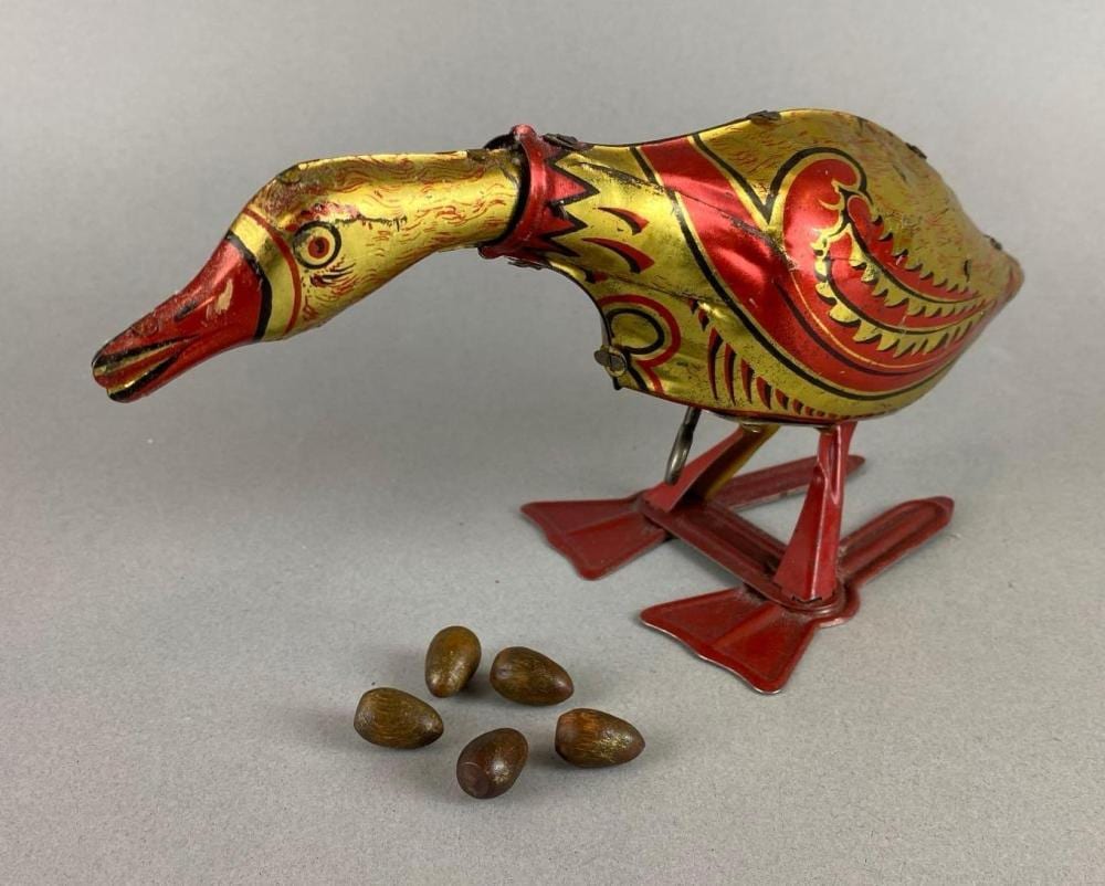 Wind-up tin lithograph toy bird with a long beak and red-and-yellow painted body, standing on red metal feet.