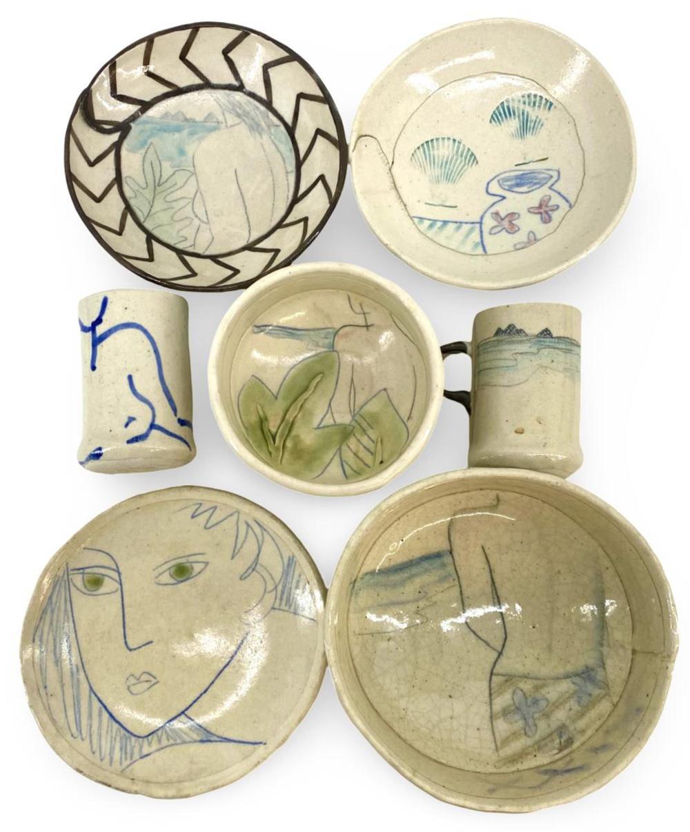 Set of seven small ceramic stoneware dishes and cups with painted designs, including faces, plants, and shells, photographed on a white background.