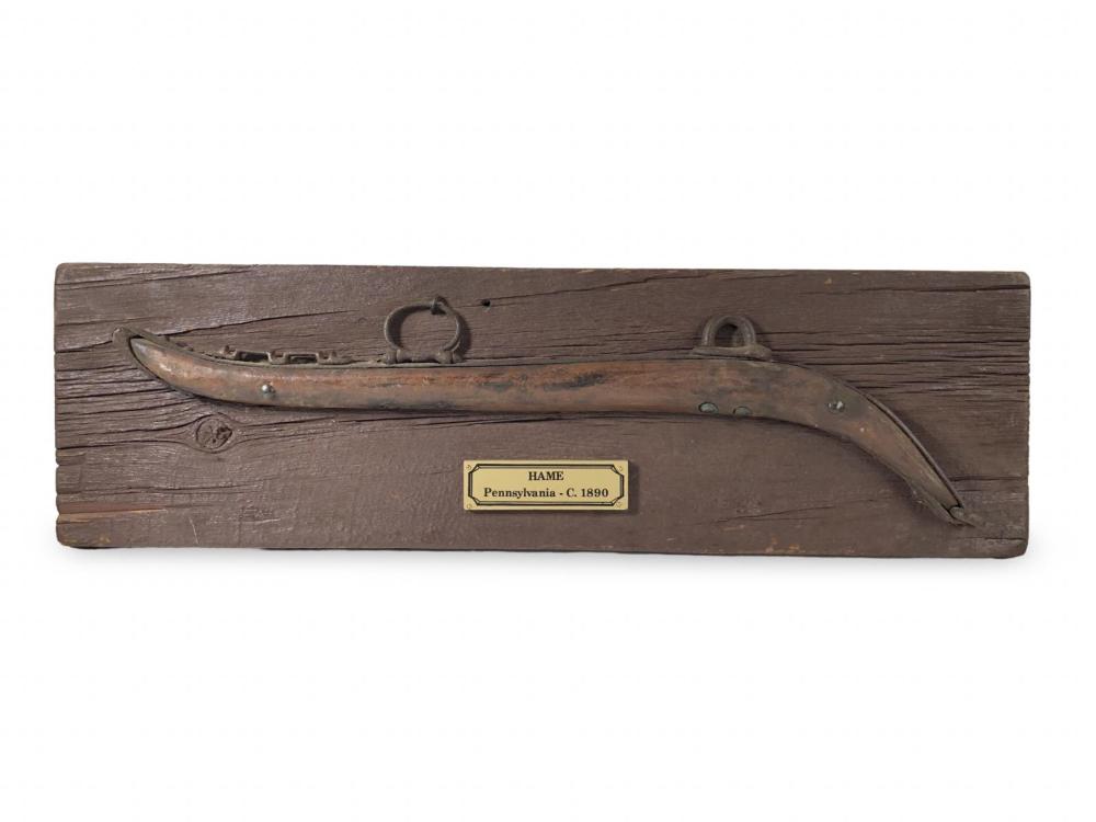 Antique wooden horse harness piece with an attached curved metal blade and iron rings, labeled “HAME”.