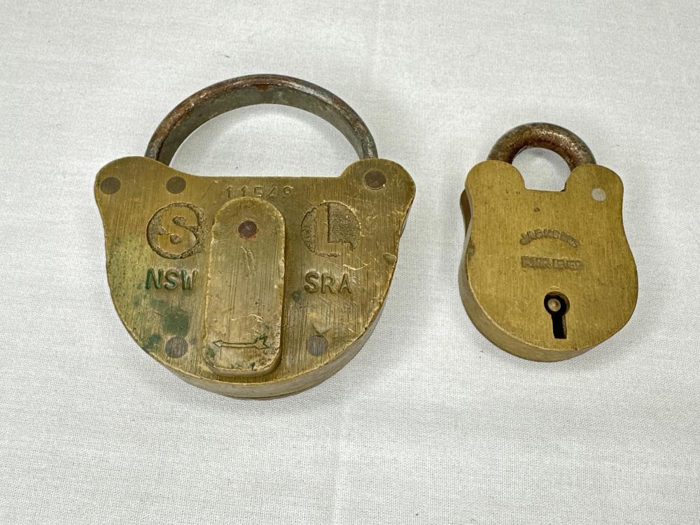 Two brass padlocks side by side, one open with a visible circular keyhole, both stamped with letters and numbers on the front.