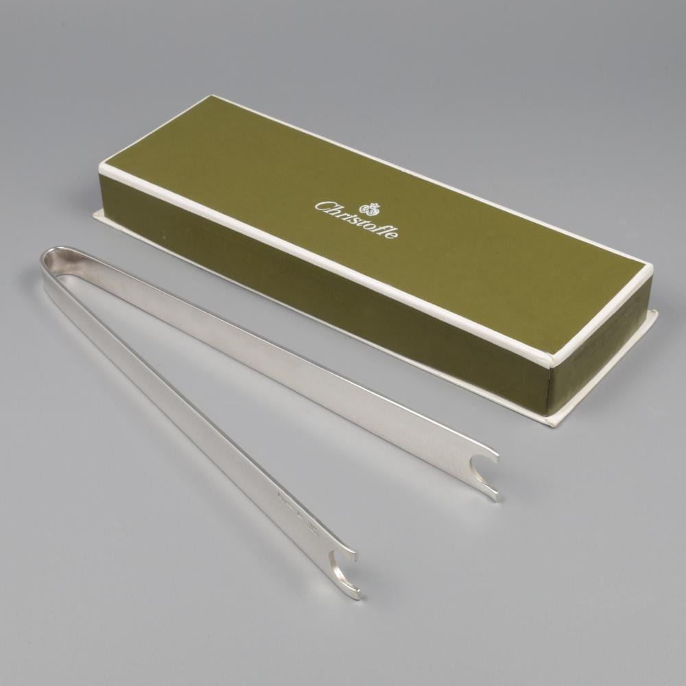 Silver metal ice tongs set with two tong arms in front of a green presentation box with a white “Christofle” logo.