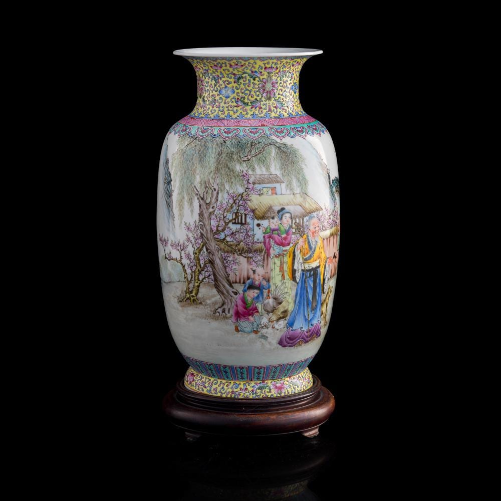 Chinese style porcelain vase with a flared rim, painted with people in a garden among flowering trees and decorative borders in blue, pink, and green.