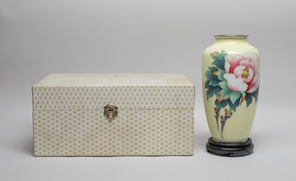 Cream ceramic vase on a dark circular base with large pink flowers and dark green leaves painted on the front.