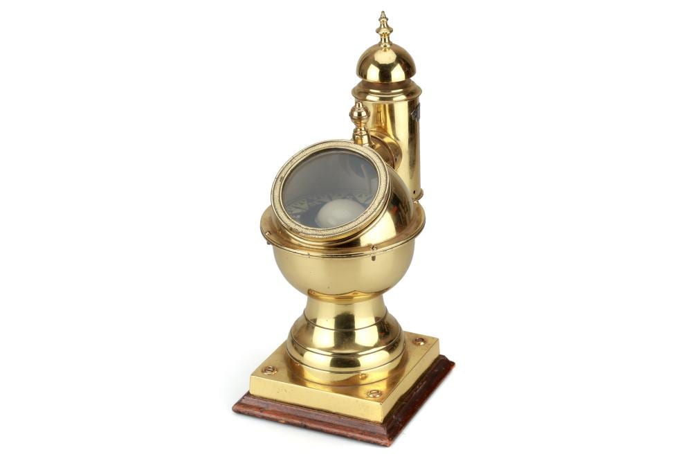 Brass yacht binnacle with a round glass compass window on a wooden base.